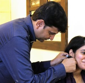 A man assists a woman by placing an earpiece in her ear, showcasing her earlobe hole piercing in Mumbai.jpg